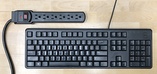keyboard next to a power strip on a desktop