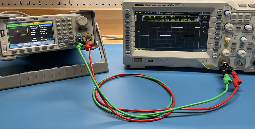 waveform generator connected to an oscilloscope with red and green wires